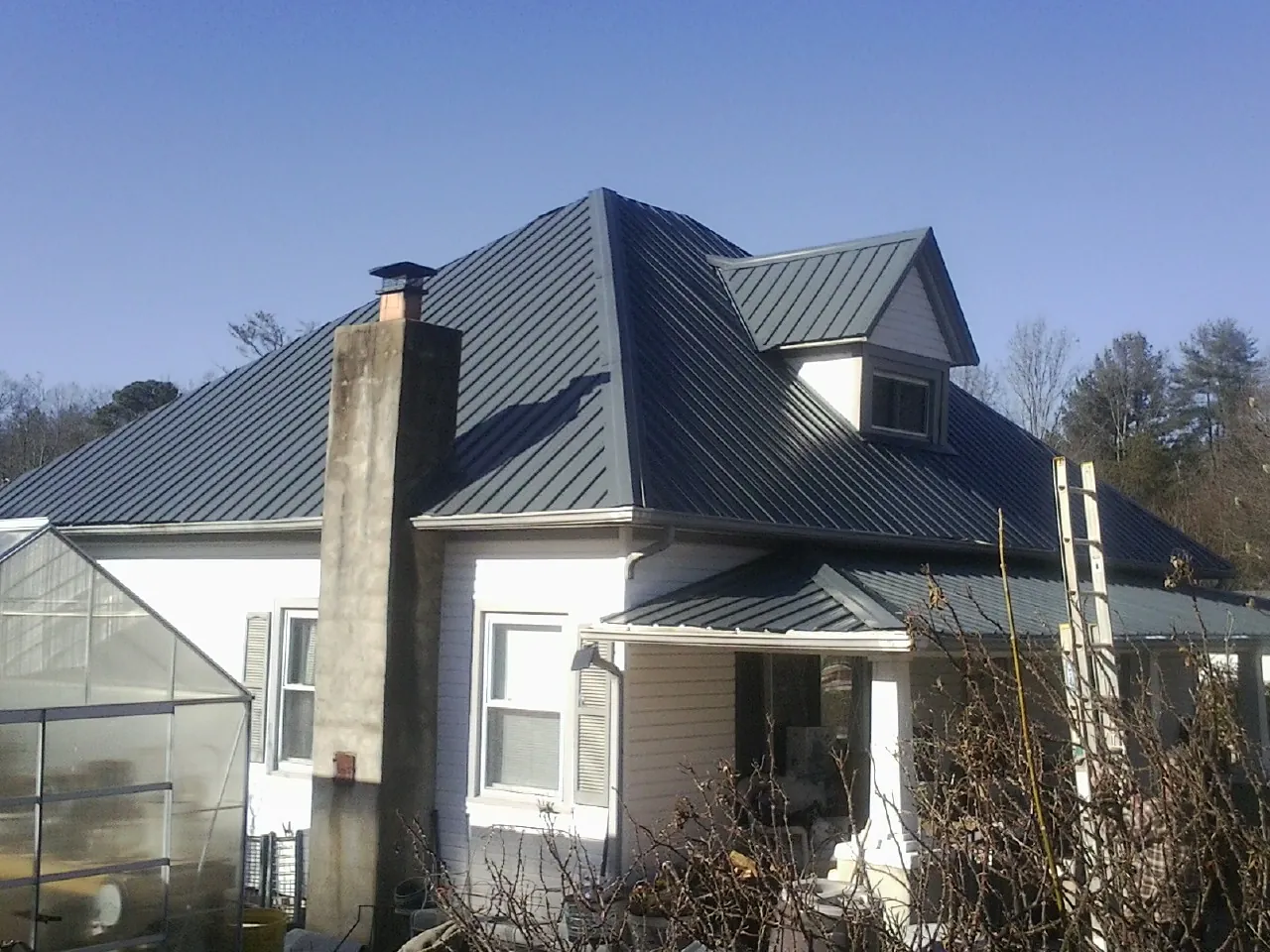 Dark blue standing seam metal roof on a white farmhouse with dormer — Slate & Tile Roof Repair by Roofing Brothers in Watkinsville