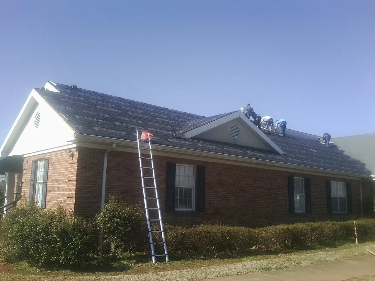 Crew tearing shingles off a brick ranch roof with a ladder set — Emergency Roof Repair work by our crew in Watkinsville