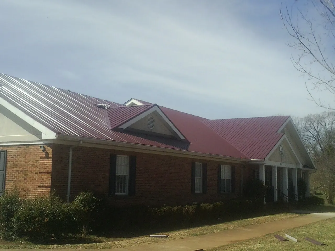 Red metal roof with gabled entries on a long brick building, from a Hail Damage Roof Repair job in Watkinsville