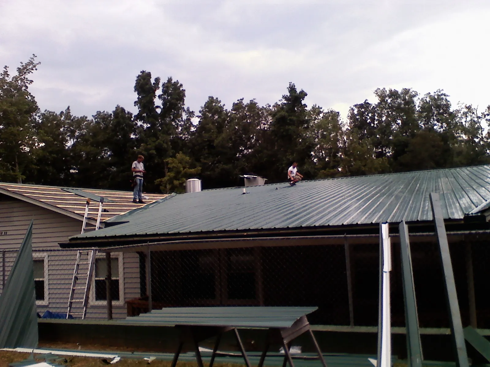 Two roofers installing green metal panels above a covered porch in Watkinsville