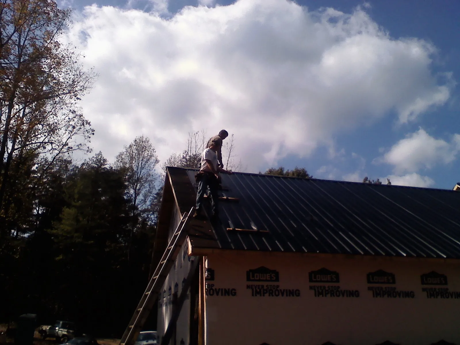 Roofer fastening dark metal panels high against a cloudy sky, from a Roof Inspection job in Watkinsville
