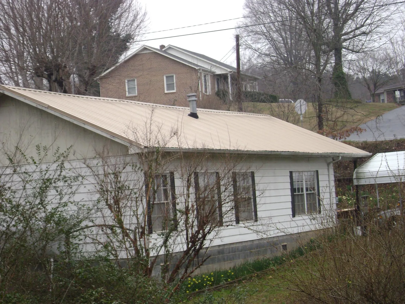 Tan metal roof on a white sided house set into a hillside — Commercial Roofing by Roofing Brothers in Watkinsville