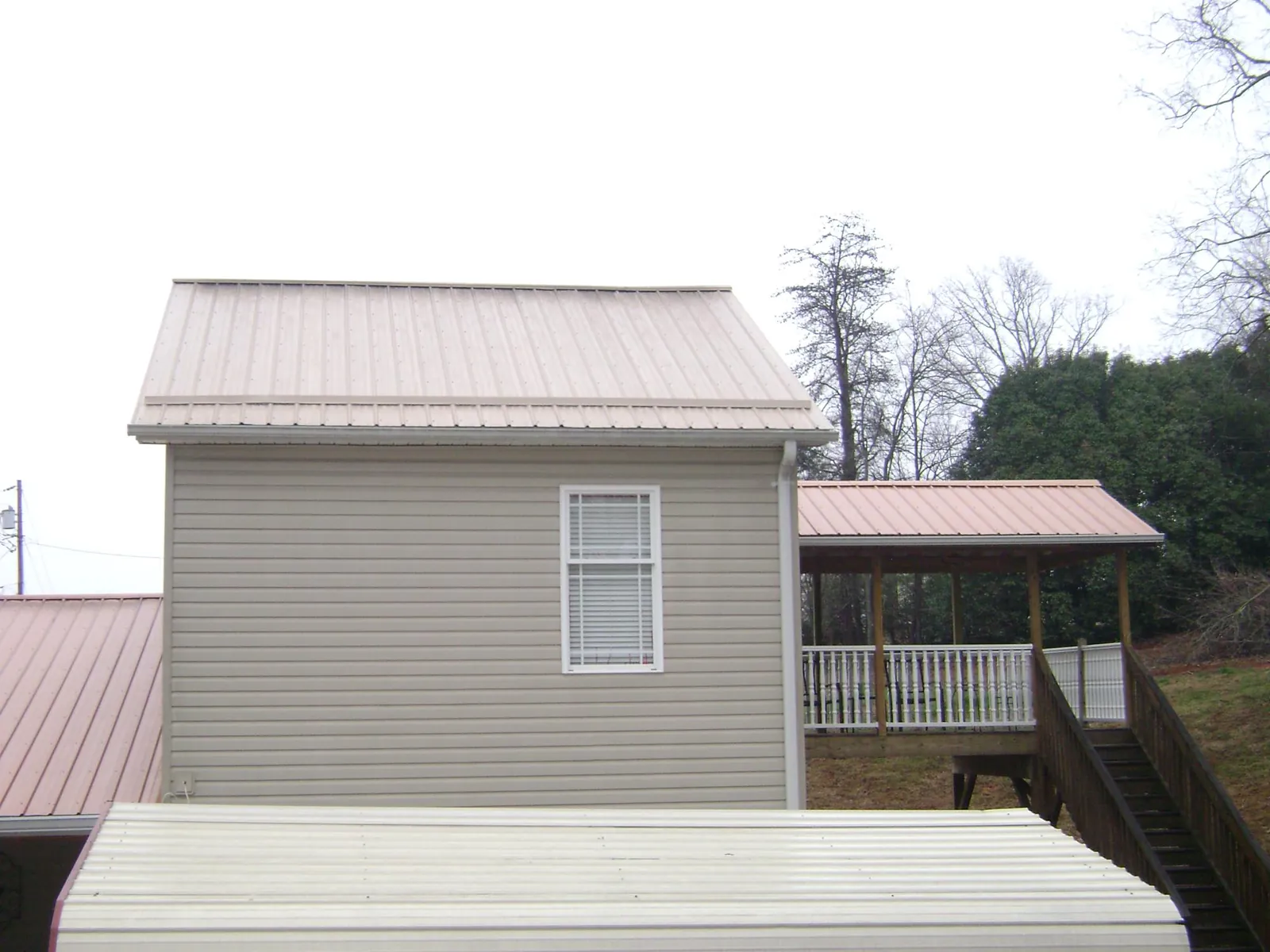 Tan metal roofs on a two story addition and attached porch, from a Roof Replacement job in Watkinsville